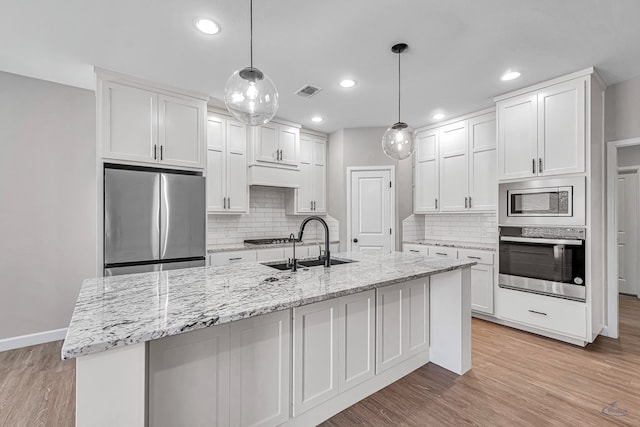 kitchen featuring appliances with stainless steel finishes, a center island with sink, and white cabinets