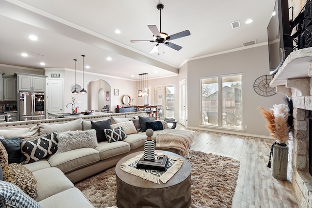 living room featuring crown molding, light hardwood / wood-style flooring, a stone fireplace, and ceiling fan