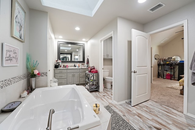 bathroom with vanity, a skylight, hardwood / wood-style flooring, toilet, and tiled bath