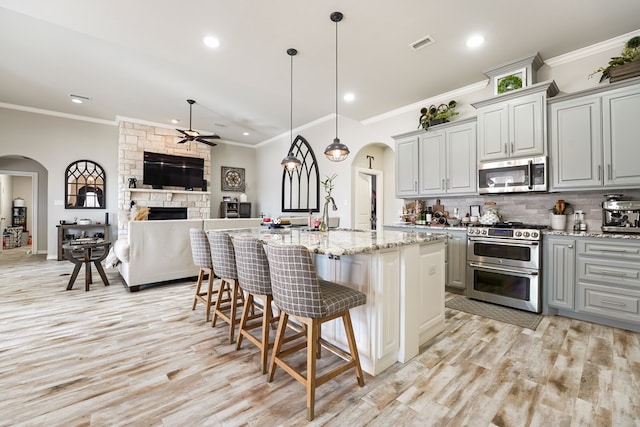 kitchen with stainless steel appliances, a center island with sink, a breakfast bar area, and gray cabinets