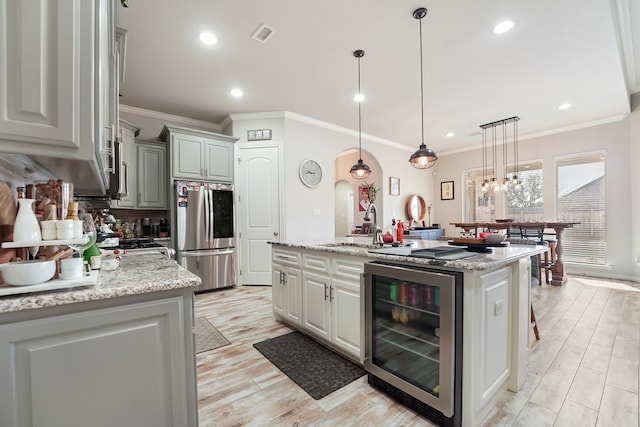 kitchen featuring decorative light fixtures, wine cooler, stainless steel fridge, light stone counters, and a center island with sink