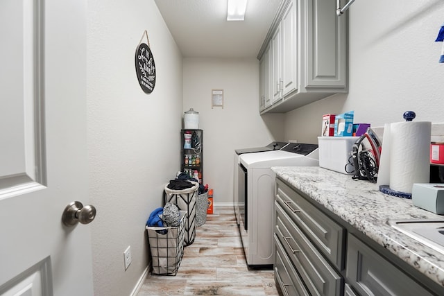 clothes washing area with light hardwood / wood-style floors, cabinets, and washing machine and clothes dryer