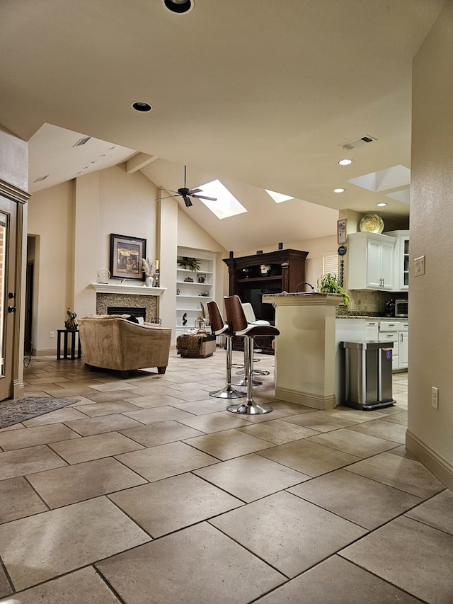 interior space with white cabinetry, ceiling fan, built in features, a kitchen bar, and vaulted ceiling with skylight