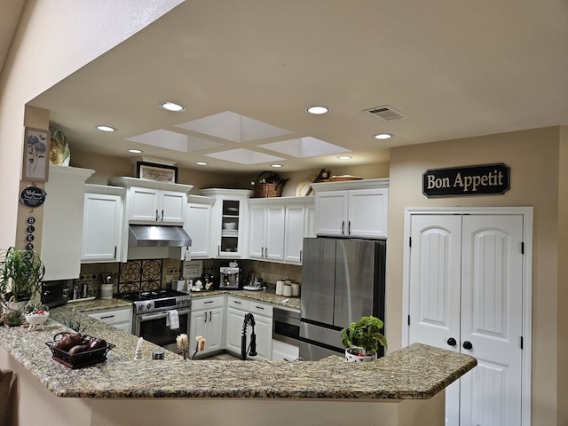 kitchen with kitchen peninsula, appliances with stainless steel finishes, white cabinets, and decorative backsplash