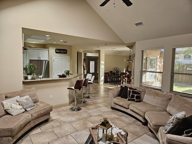 tiled living room featuring ceiling fan with notable chandelier and high vaulted ceiling