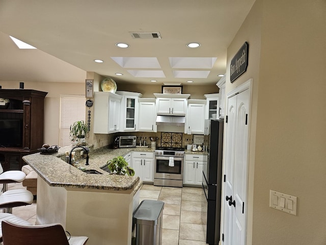 kitchen featuring decorative backsplash, kitchen peninsula, stainless steel range, sink, and a breakfast bar area