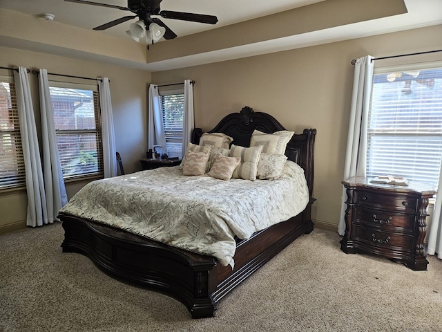 carpeted bedroom featuring a raised ceiling, multiple windows, and ceiling fan