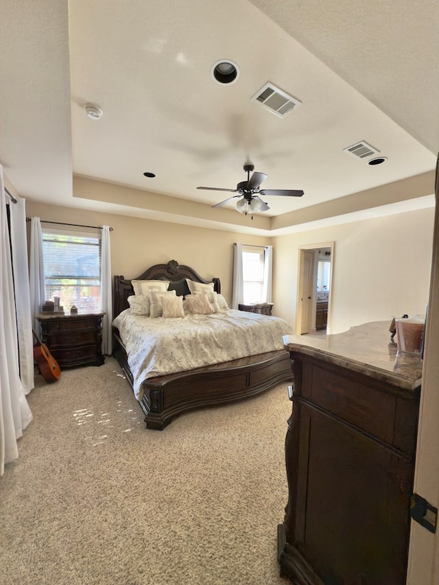 bedroom with light colored carpet, ceiling fan, and a tray ceiling