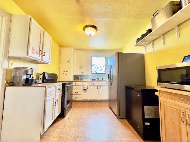 kitchen with light parquet flooring, white cabinets, stainless steel appliances, and a textured ceiling