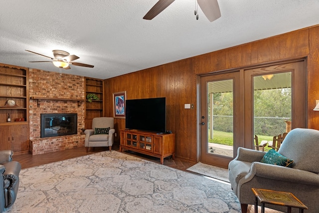 living room featuring a brick fireplace, built in features, light hardwood / wood-style flooring, a textured ceiling, and wooden walls