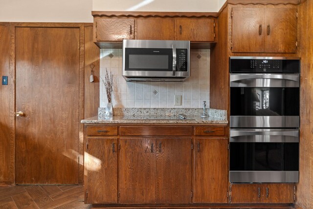 kitchen featuring appliances with stainless steel finishes, dark parquet floors, tasteful backsplash, and light stone counters