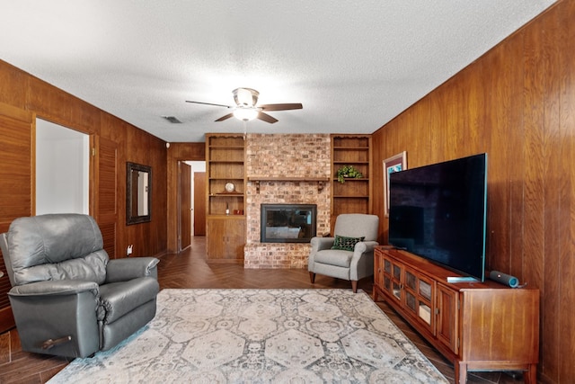 living room with built in shelves, dark parquet flooring, a textured ceiling, and a brick fireplace