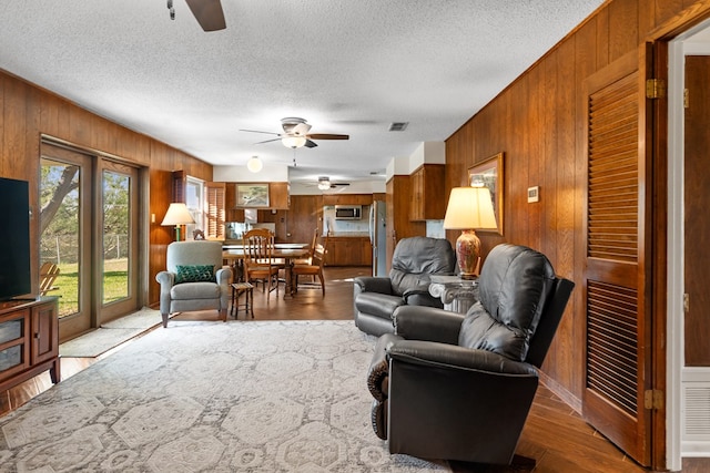 living room with hardwood / wood-style floors, ceiling fan, and wooden walls