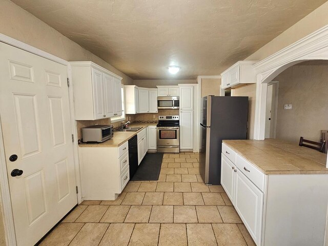 kitchen with light countertops, a sink, white cabinetry, appliances with stainless steel finishes, and arched walkways