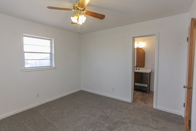 unfurnished bedroom with dark colored carpet, ensuite bathroom, and ceiling fan