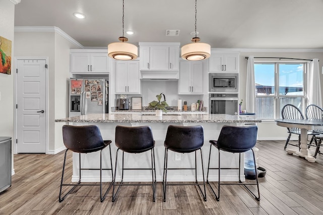 4107 Connally St, Big Spring, TX 79720 - kitchen with appliances with stainless steel finishes, ornamental molding, white cabinetry, light wood-type flooring, and a kitchen breakfast bar