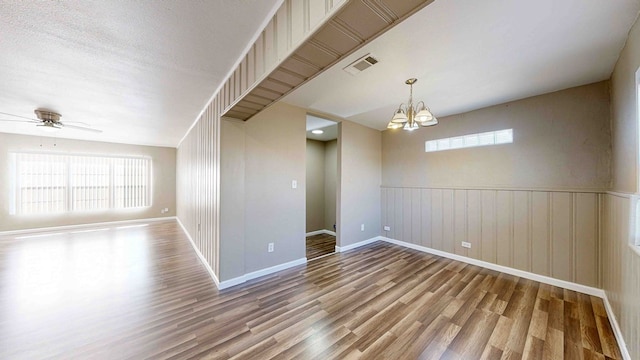 spare room featuring a textured ceiling, ceiling fan with notable chandelier, and hardwood / wood-style flooring