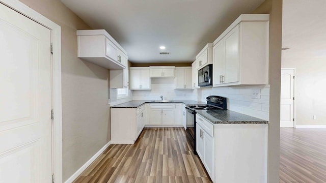 kitchen featuring backsplash, dark stone counters, black appliances, white cabinets, and light wood-type flooring