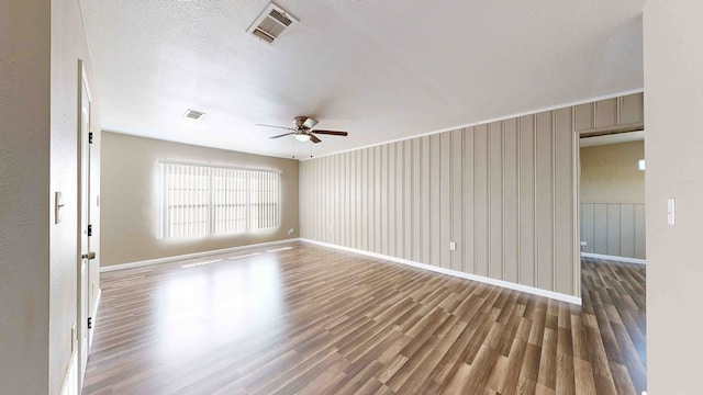 empty room featuring wood-type flooring, a textured ceiling, ceiling fan, and wood walls