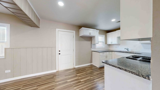 kitchen with tasteful backsplash, light hardwood / wood-style flooring, dark stone countertops, black stovetop, and white cabinets