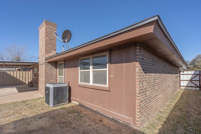 view of home's exterior featuring brick siding, central AC unit, fence, and a lawn