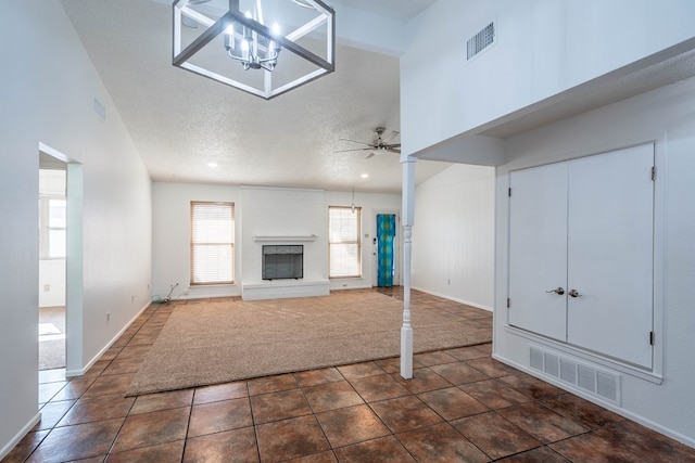 unfurnished living room featuring tile patterned floors, a fireplace with raised hearth, visible vents, and a textured ceiling