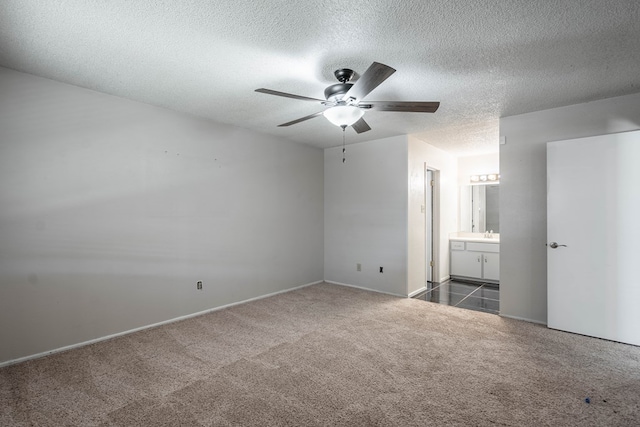 unfurnished bedroom featuring ceiling fan, a sink, a textured ceiling, dark colored carpet, and connected bathroom