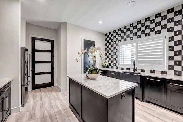 kitchen with light stone counters, a sink, freestanding refrigerator, a kitchen island, and wood finish floors