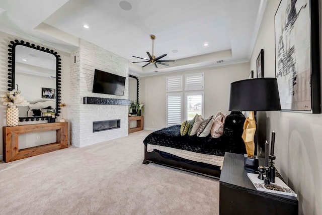 carpeted bedroom featuring a stone fireplace, a tray ceiling, and recessed lighting