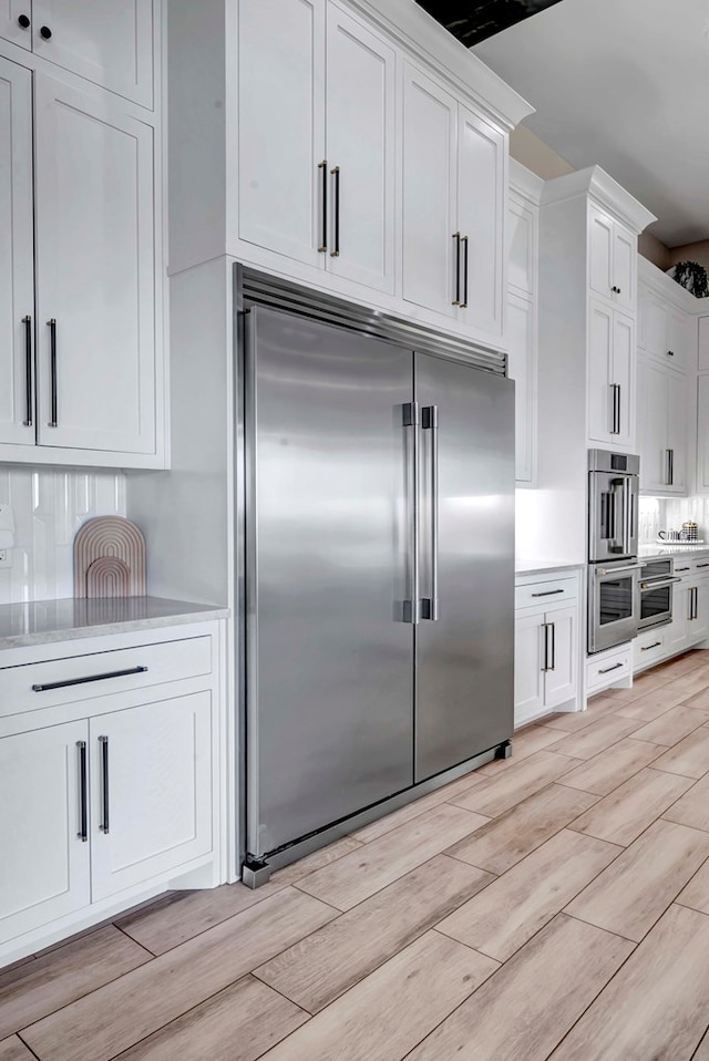 kitchen featuring light countertops, stainless steel built in refrigerator, white cabinetry, and light wood-style flooring