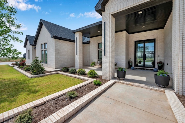 view of exterior entry with a lawn, brick siding, and a patio