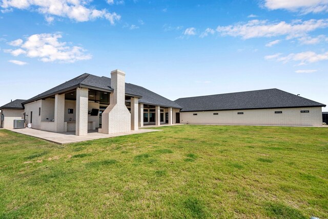 back of house with a patio area, a chimney, central air condition unit, a lawn, and brick siding