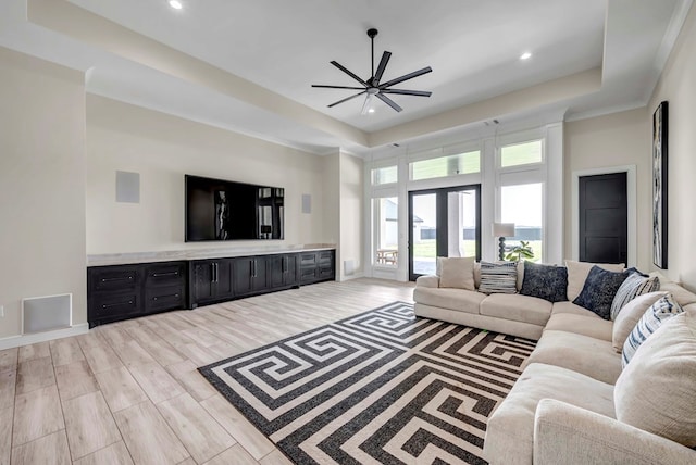 living area with light wood-type flooring, a raised ceiling, ceiling fan, and recessed lighting