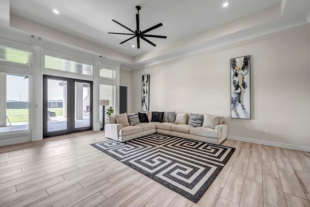 living room with a raised ceiling, wood finished floors, a healthy amount of sunlight, and ceiling fan