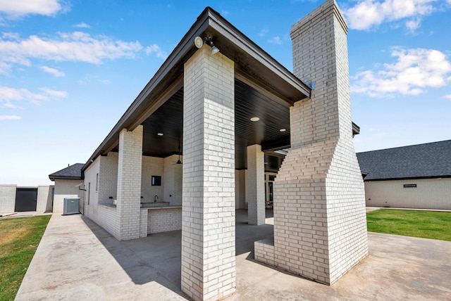 view of property exterior featuring exterior kitchen, central AC unit, a chimney, brick siding, and a patio area