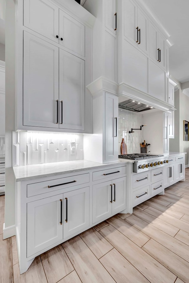 kitchen featuring white cabinets, backsplash, light stone countertops, stainless steel gas cooktop, and wood finish floors