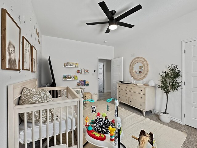 carpeted bedroom with ceiling fan and a crib