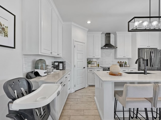 kitchen with pendant lighting, white cabinets, sink, wall chimney exhaust hood, and stainless steel fridge with ice dispenser