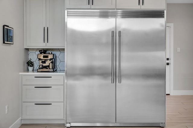 kitchen with baseboards, stainless steel built in fridge, light countertops, light wood-type flooring, and backsplash