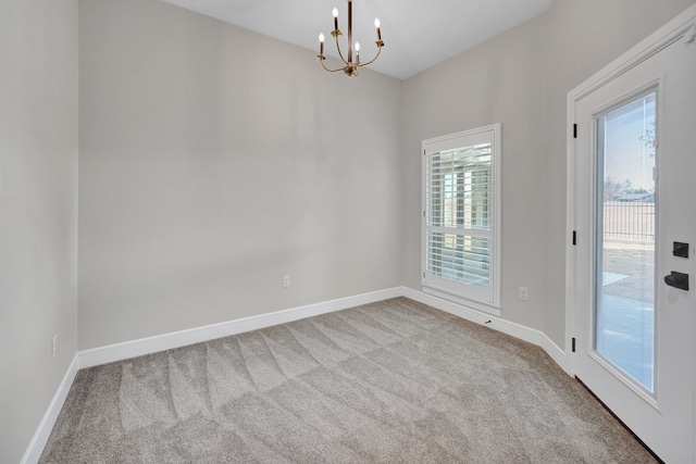 spare room featuring a chandelier, baseboards, carpet flooring, and a healthy amount of sunlight