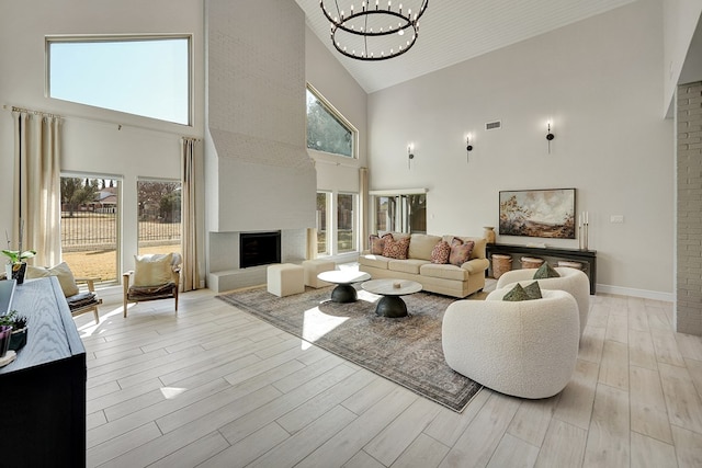 living area featuring visible vents, baseboards, light wood-style floors, a fireplace, and a chandelier