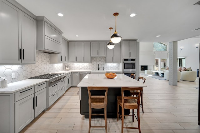 kitchen featuring open floor plan, a center island, stainless steel appliances, gray cabinets, and a sink