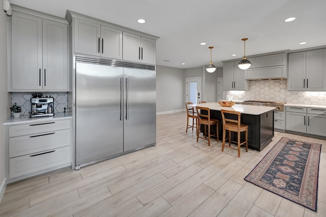 kitchen featuring light wood finished floors, a kitchen breakfast bar, stainless steel built in refrigerator, light countertops, and gray cabinetry