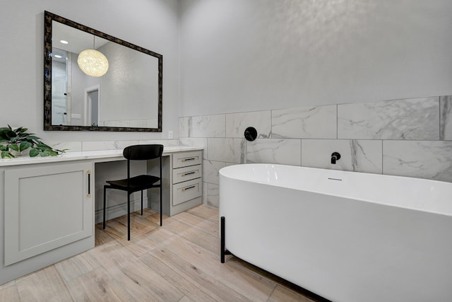 full bathroom featuring tile walls, wainscoting, vanity, wood finished floors, and a freestanding tub