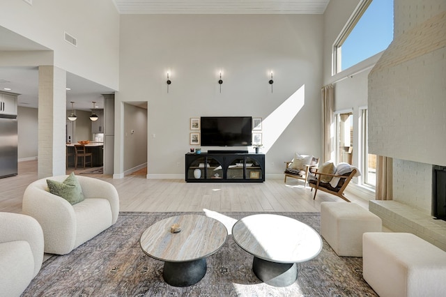 living room featuring a fireplace, a towering ceiling, light wood-style flooring, and baseboards