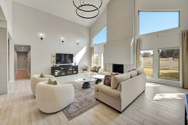 living room with high vaulted ceiling, a fireplace, baseboards, light wood-style floors, and an inviting chandelier