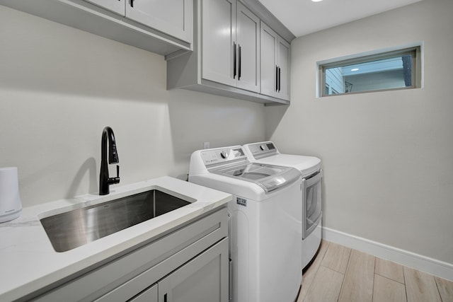 washroom with a sink, baseboards, washer and dryer, cabinet space, and light wood finished floors