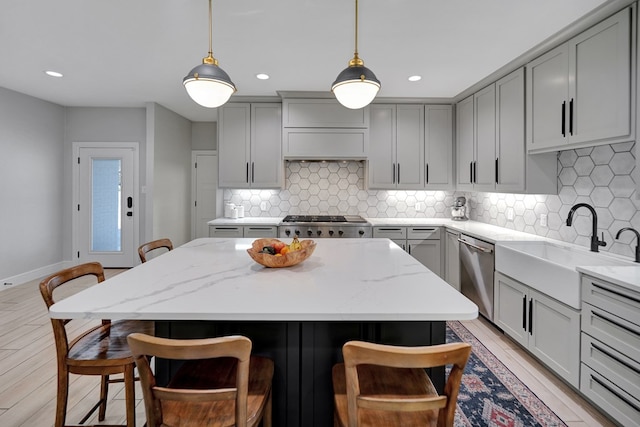 kitchen with appliances with stainless steel finishes, a breakfast bar, a sink, and gray cabinetry