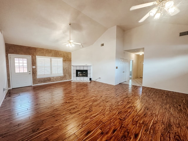 unfurnished living room with high vaulted ceiling, hardwood / wood-style flooring, a tile fireplace, and ceiling fan