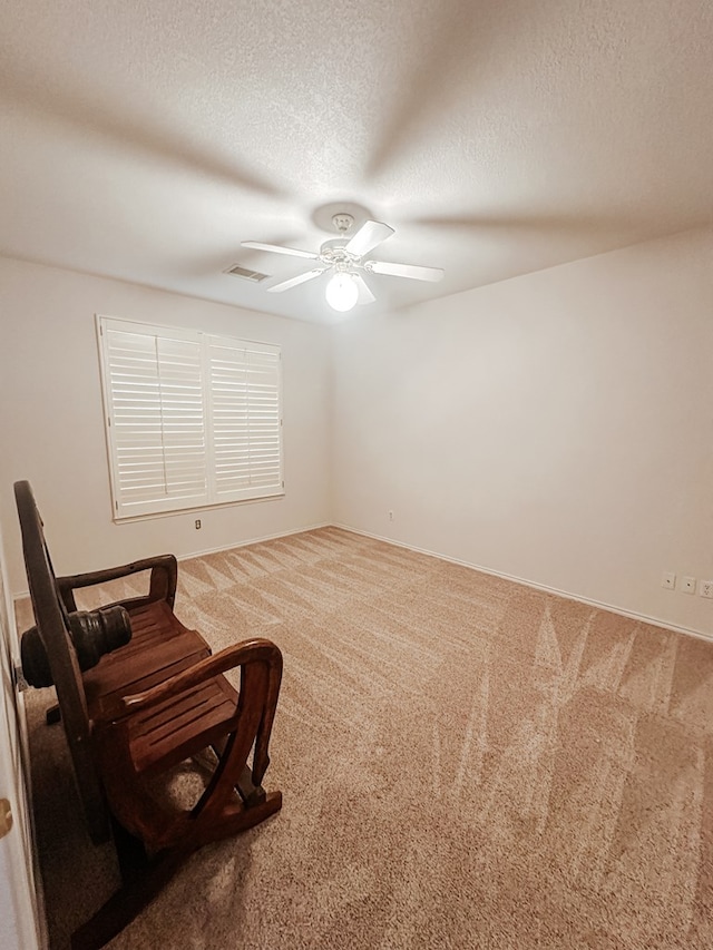 living area featuring ceiling fan, carpet floors, and a textured ceiling